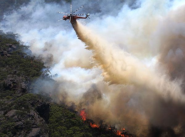A helicopter dropping water on a bushfire.