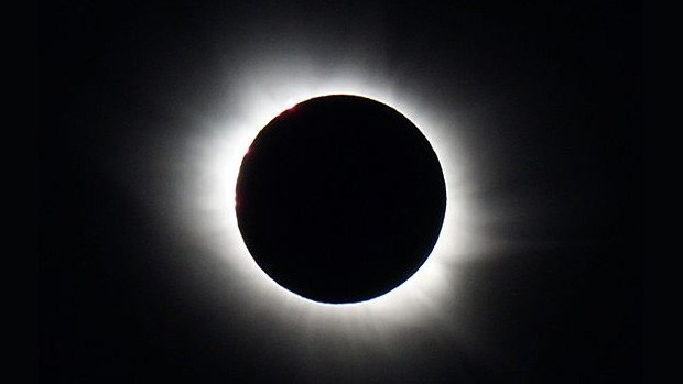 The sun during a total solar eclipse, with the outer corona visible beyond the shadow of the moon.