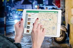Woman holding tablet in city street at night, looking at street map on screen