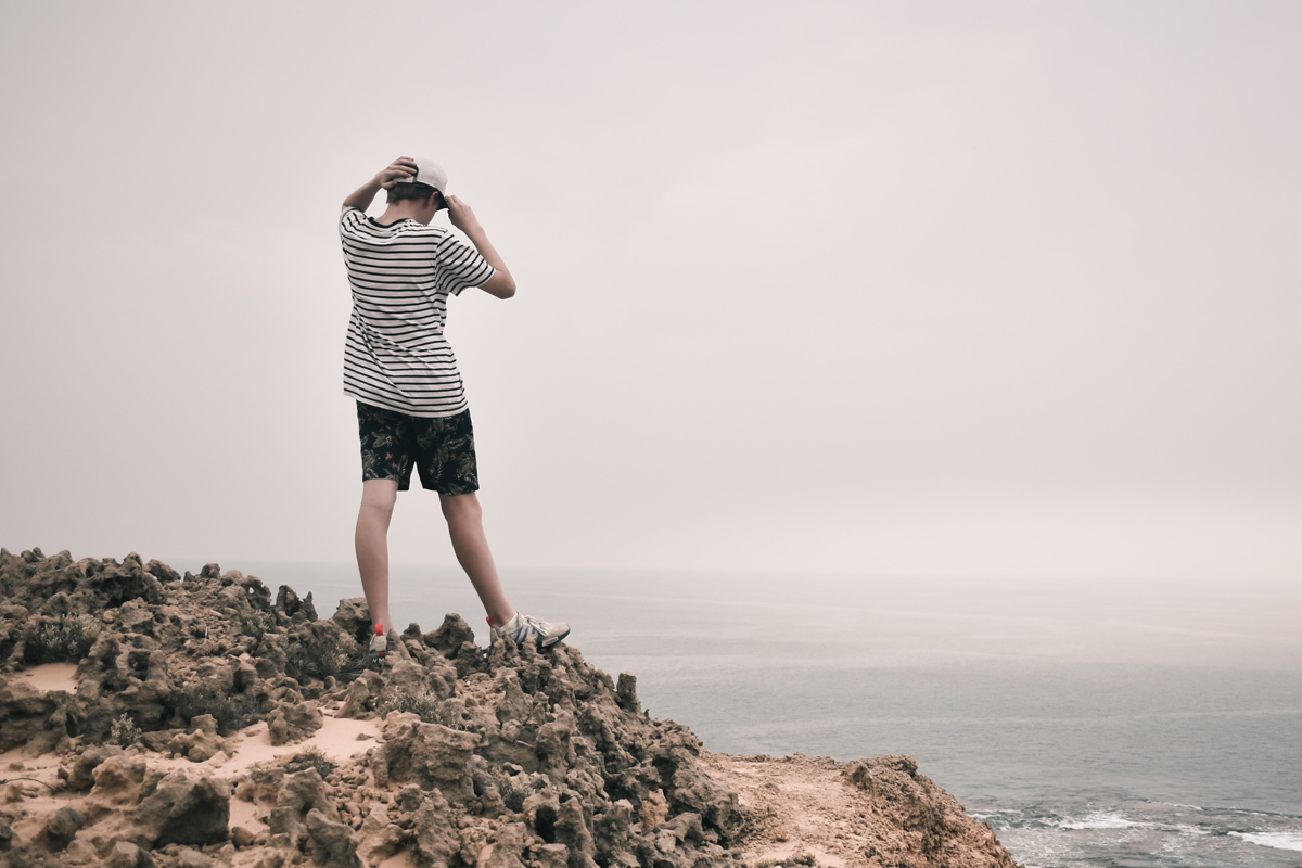 A person standing on a cliff face looking out over a body of water.