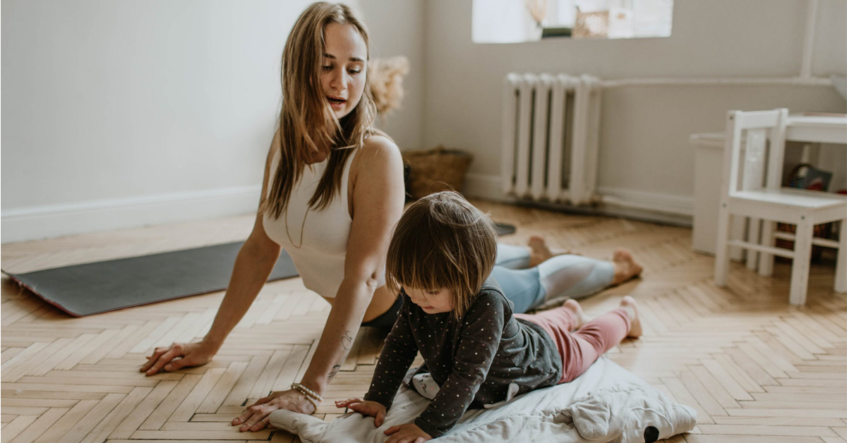 A wide angle shot of a woman and a child doing yoga on the floor inside a house.