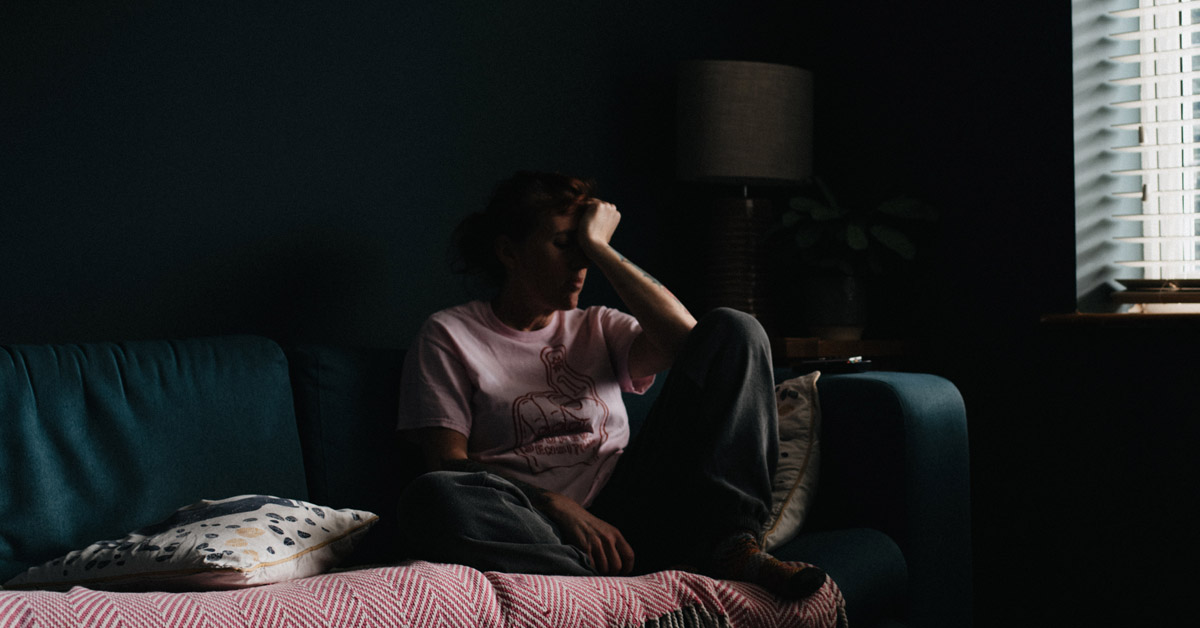 A person in a dark living room with their head in their hands.