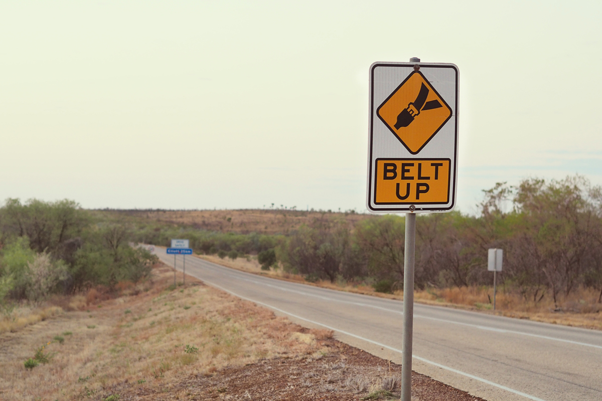 An outback road with a sign saying 'BELT UP'.