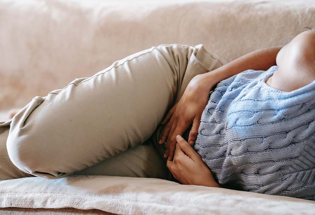 Close-up shot of a person lying on a couch holding their stomach.