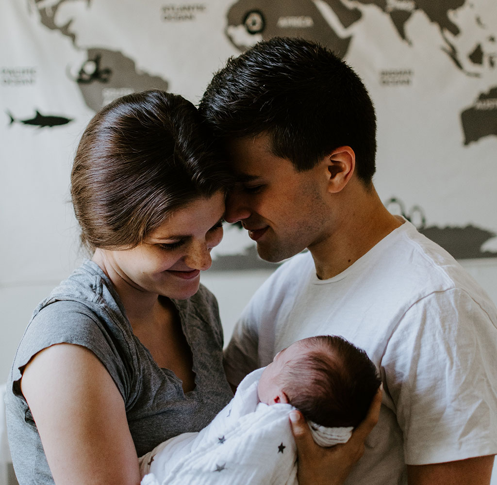 Two adults holding a baby standing in front of a world map