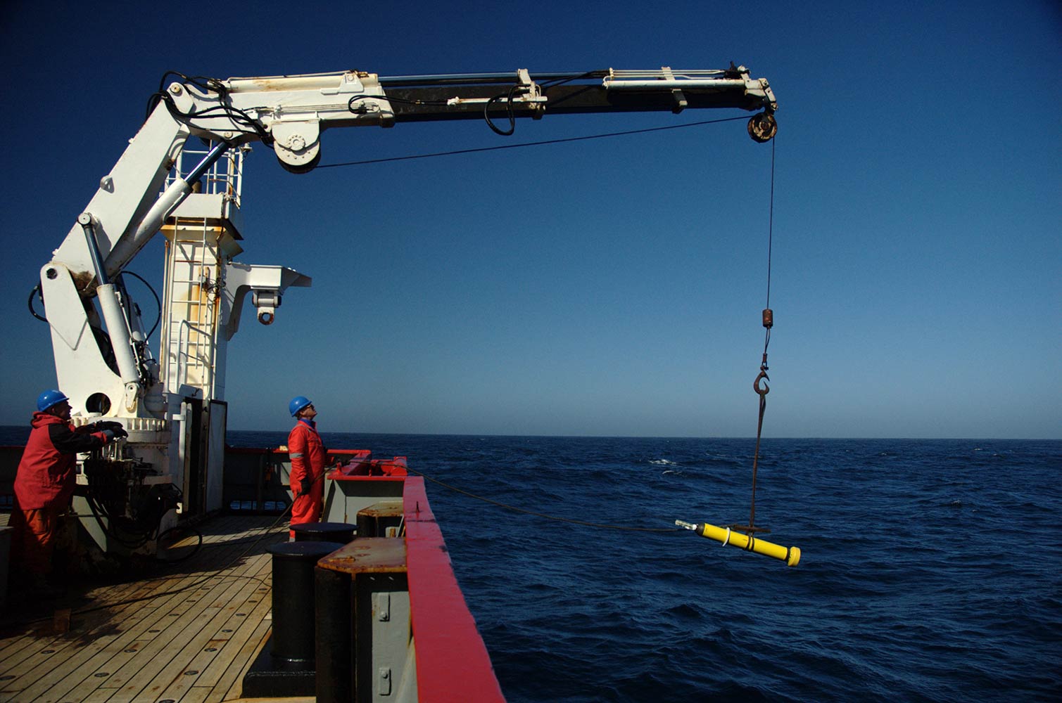 Crane on the deck of a boat lowering an ARGO Buoy into the ocean.