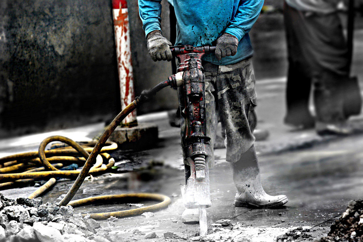 Construction worker with machinery in a city jack-hammering concrete