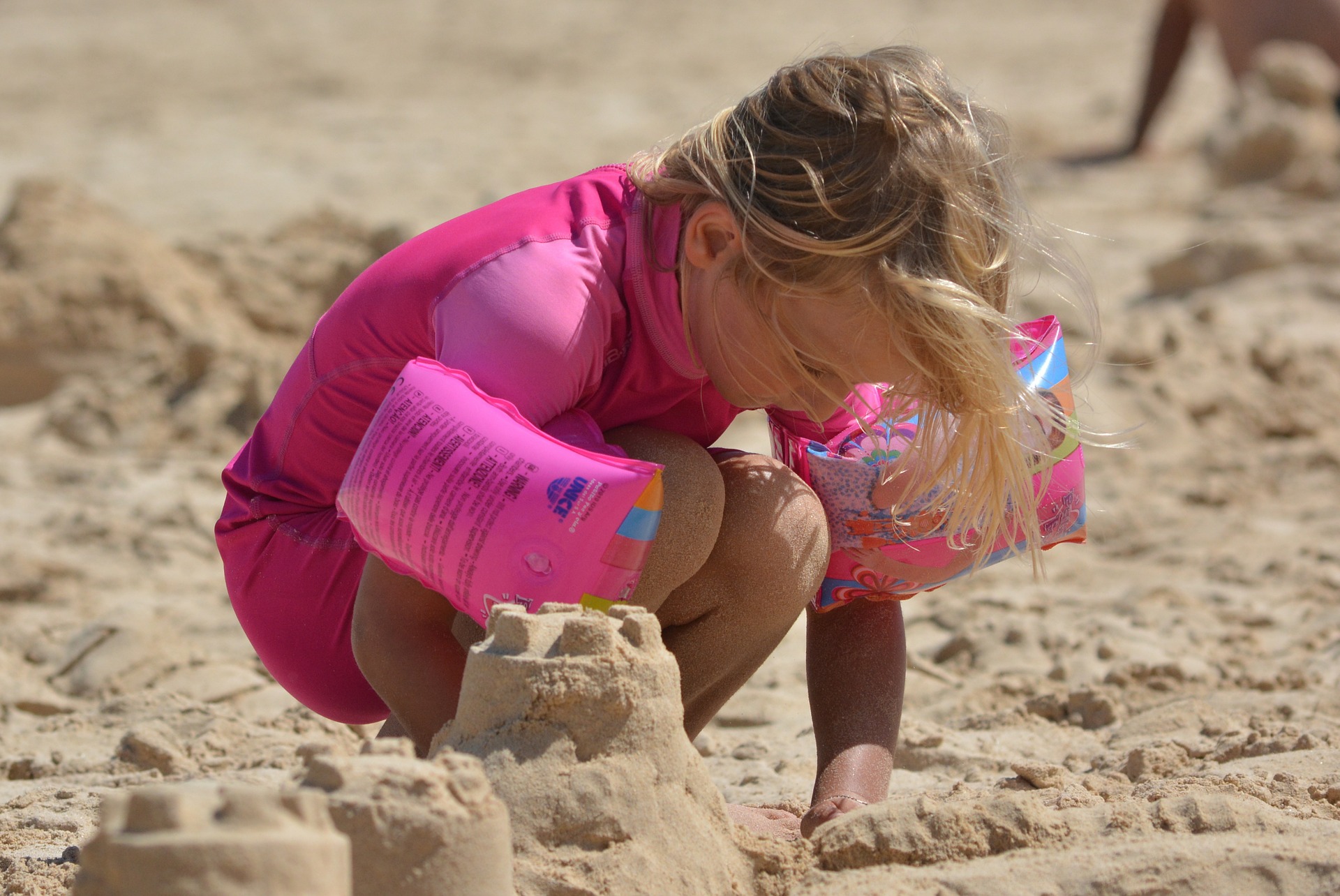 A child in pink playing in the sand building sandcastles