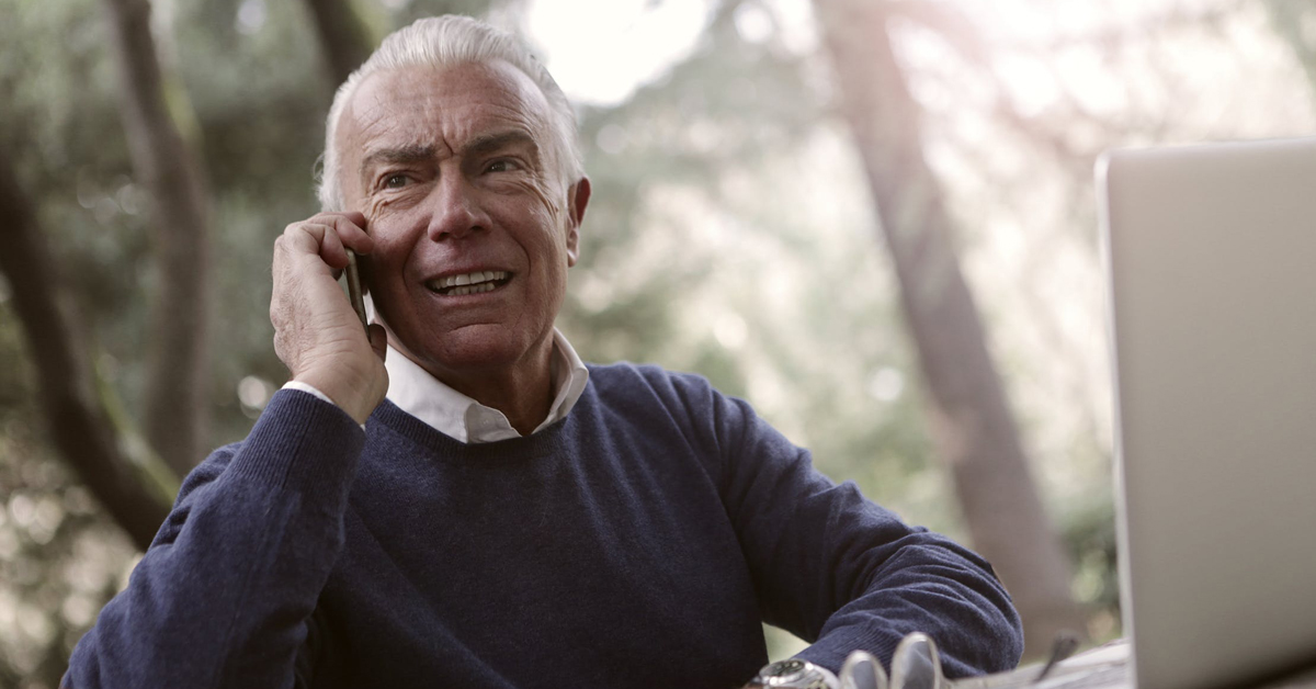 Man uses mobile phone outside with laptop.