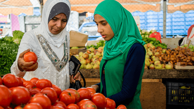 Two women examining vegetables in a market.