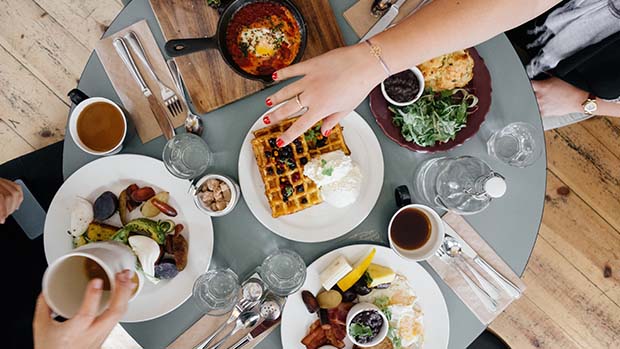 A photo taken from above of a table with food and people's hands reaching for food.