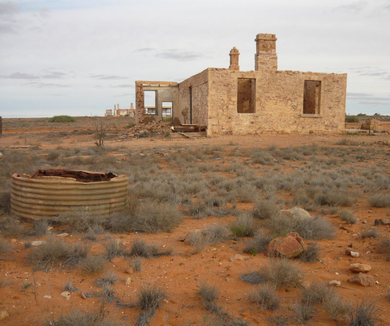 Ruins of stone buildings in a flat desert-like landscape with some low and mainly dry vegetation