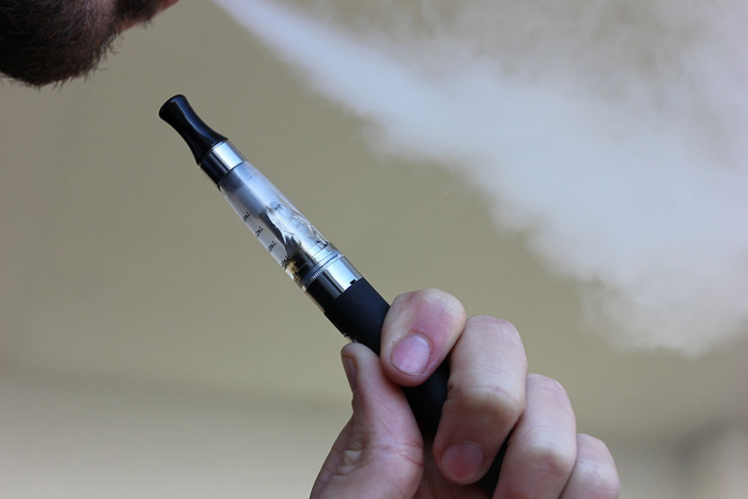 A man smoking an e-cigarette and exhaling vapour.