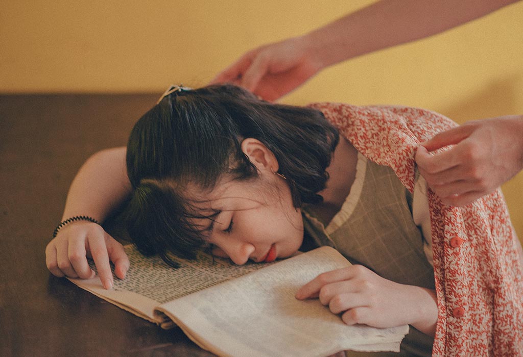 Person fallen asleep on top of a book at a desk