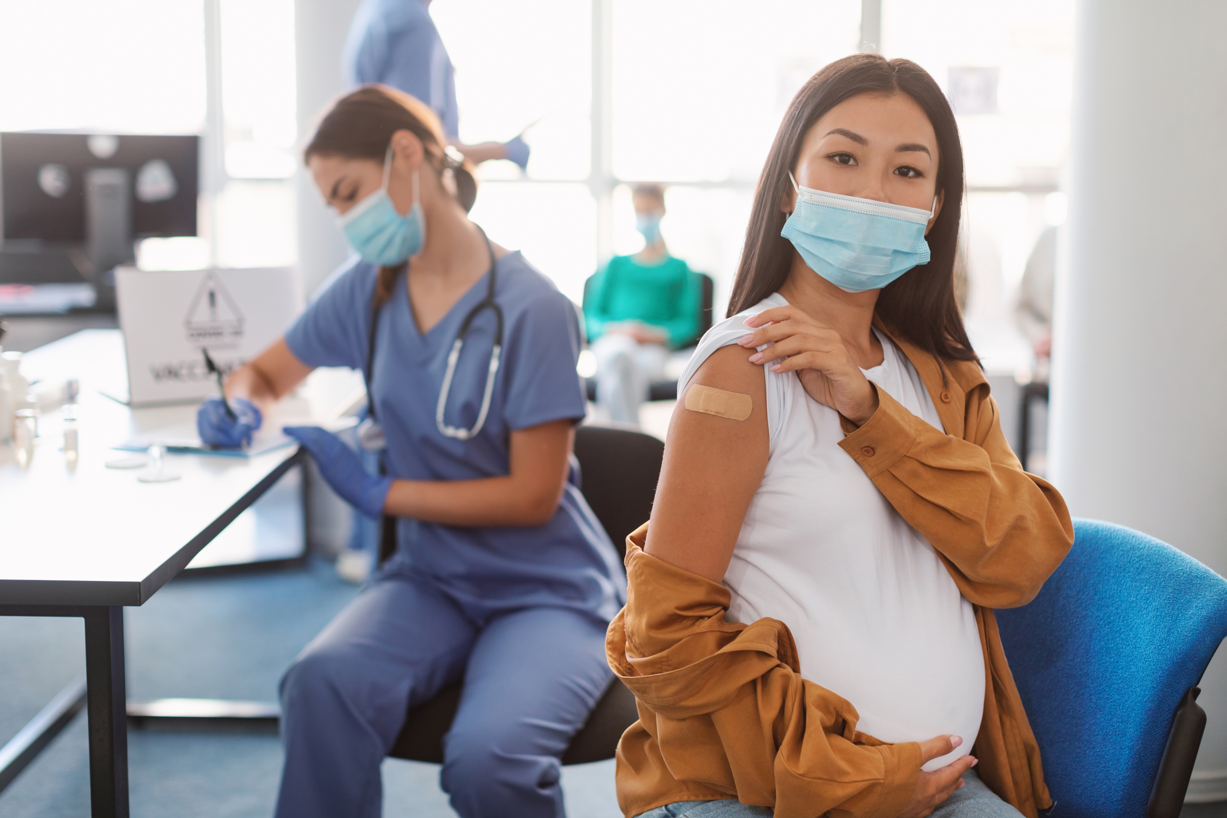 A vaccine clinic with a health profession and a pregnant person showing off a bandaid from vaccination.