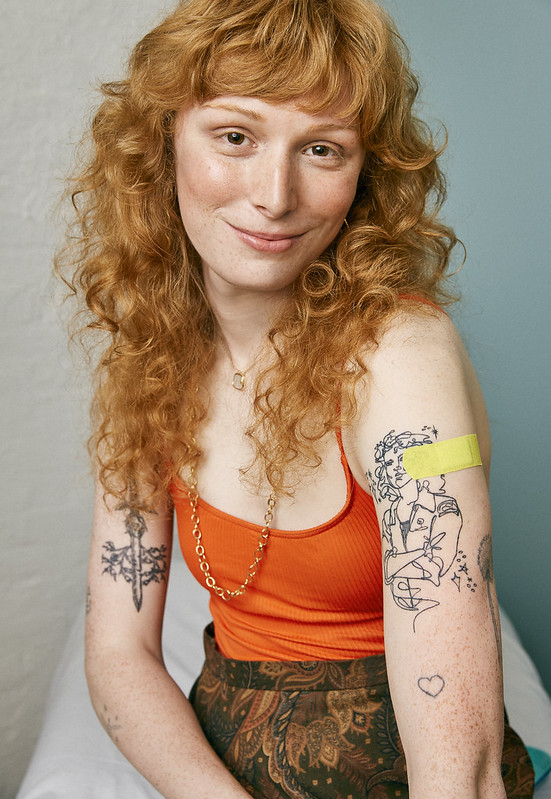 A young woman in a clinic smiling with a bandaid on her arm