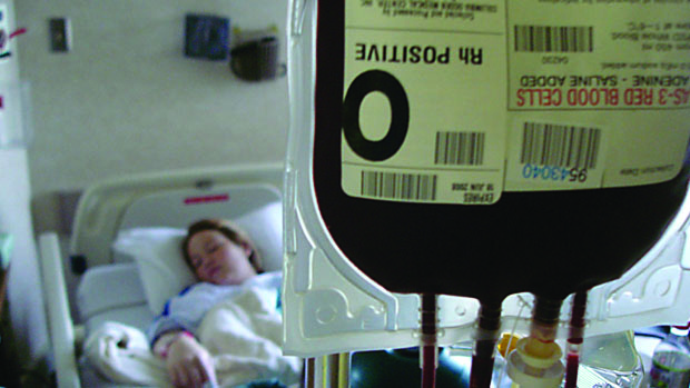 A sleeping woman in hospital hooked up to a bag of Rh positive blood.