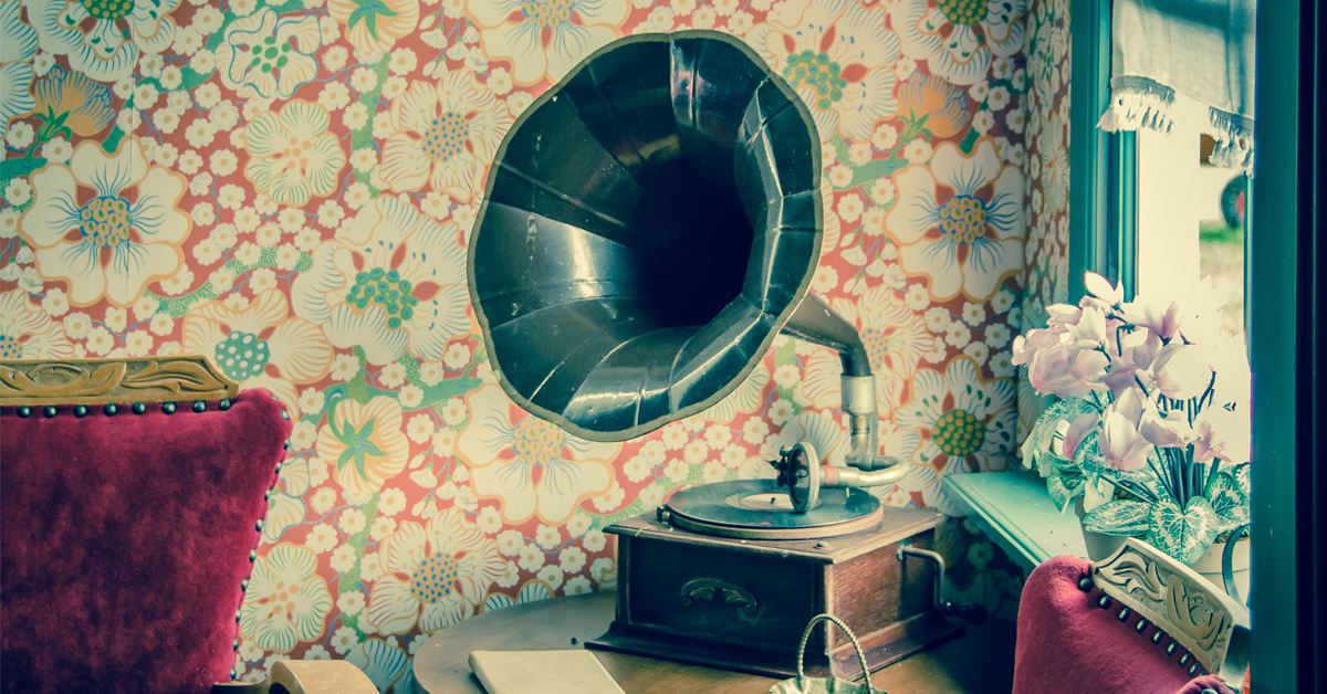 A gramophone inside a room with floral wallpaper, next to a window.