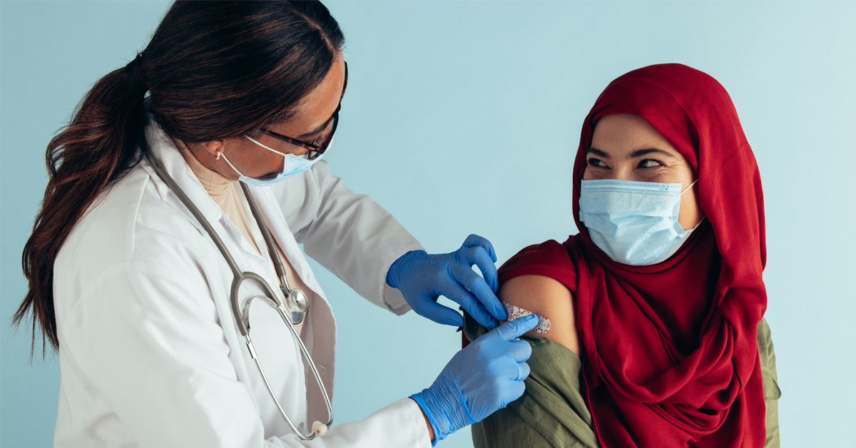 A health professional gives a smiling person wearing a mask an injection