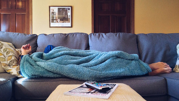 Person lying on a couch with a blanket pulled up over their head