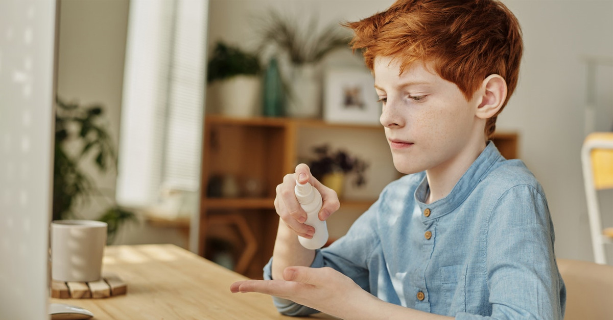 A child uses hand sanitiser at a desk