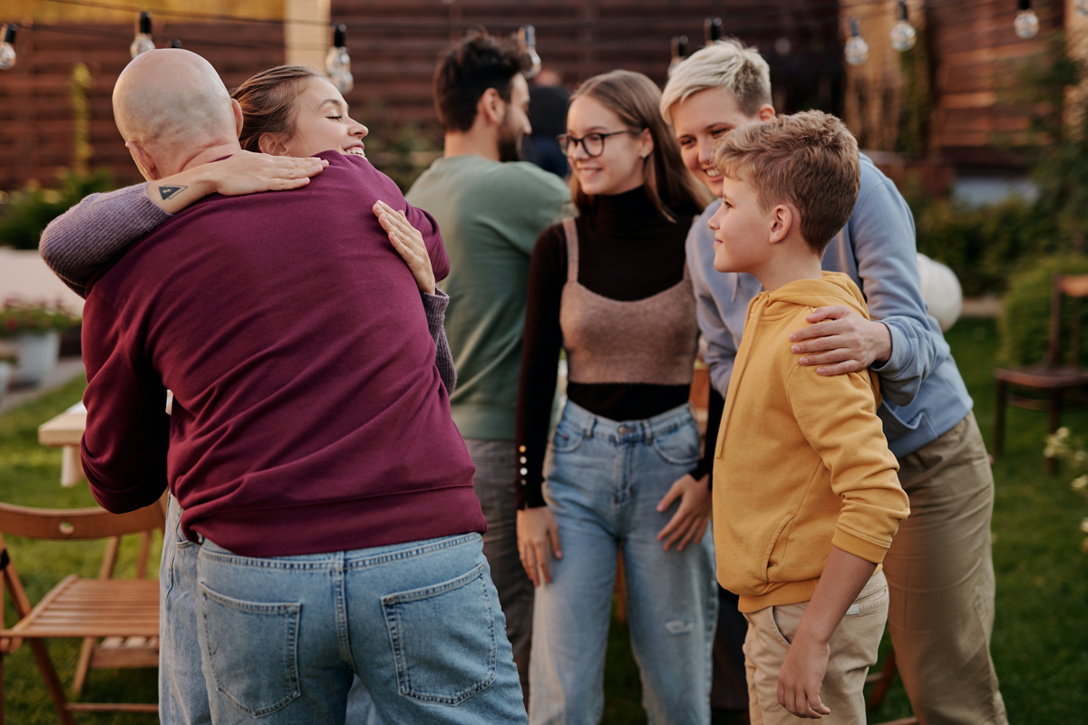 A group of people of mixed ages greeting and smiling at an outdoor barbeque