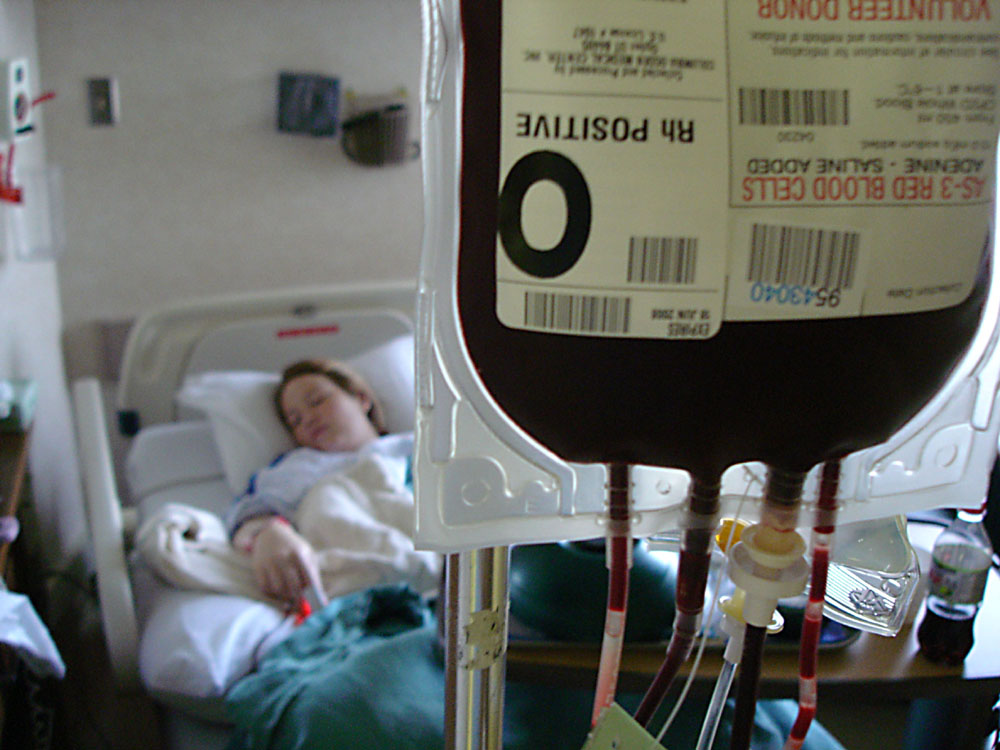 A patient lying in a hospital bed with a blood donation bag in the foreground