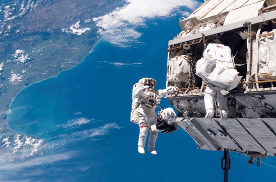 Astronauts geared up in their spacesuits during construction activity outside the International Space Station.