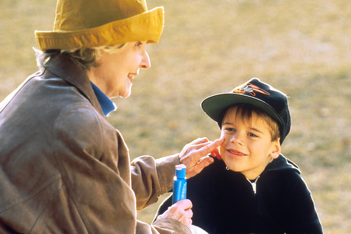 An older woman puts sunscreen on a young’s child’s face