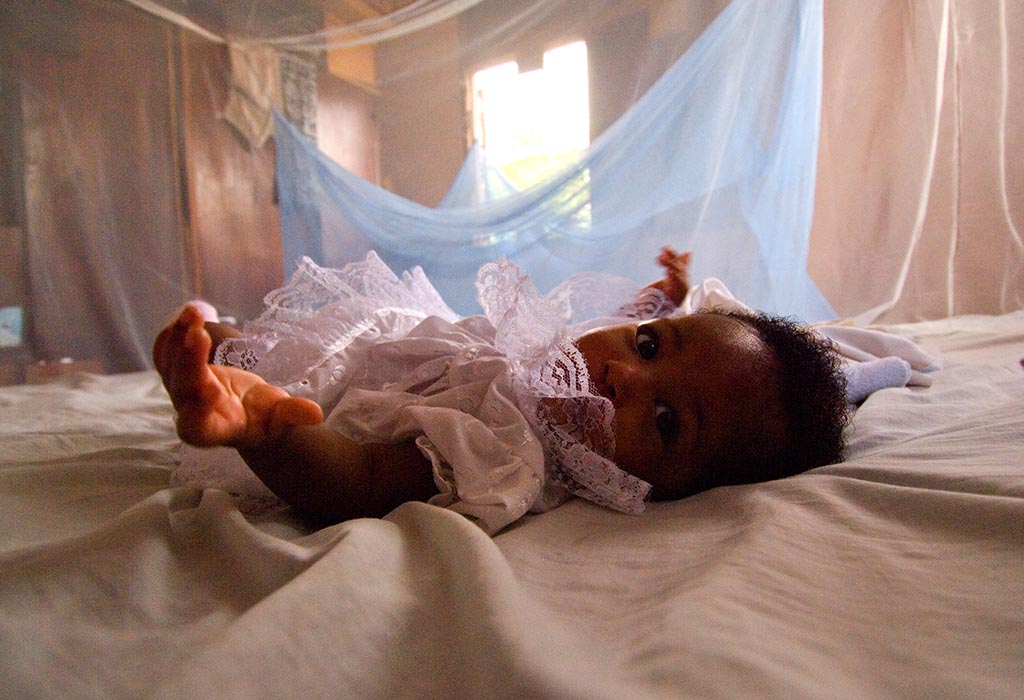 A baby, lying down, surrounded by mosquito netting