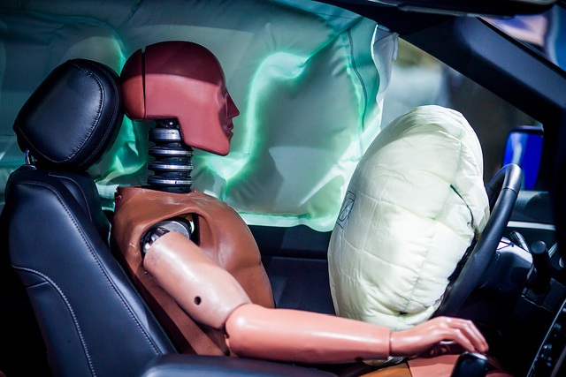 A crash test dummy in front of an inflated airbag.