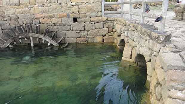 A photograph of part of a tidal mill showing a pool of water and a water wheel.