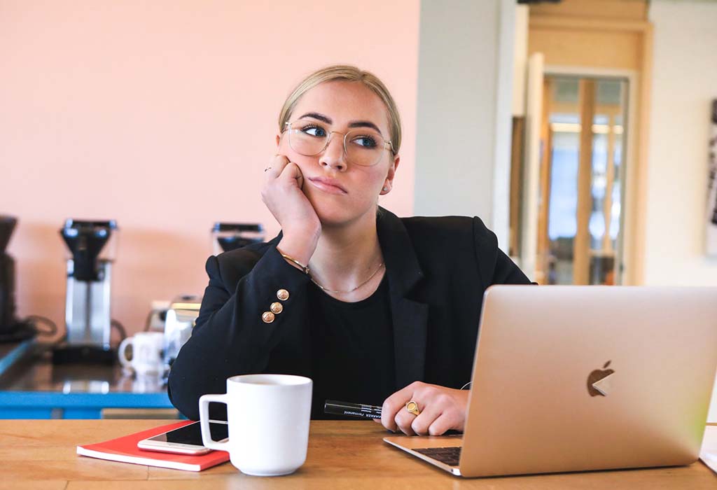 A person resting their head on one hand, sitting at a desk, thinking hard about something