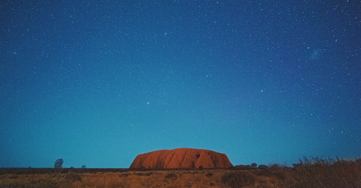 a landscape photo of Uluru, a red arkose rock, under a starry sky