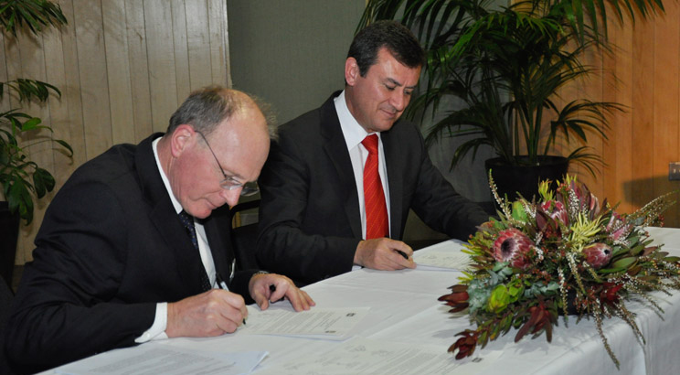 The President of the Academy and the Ambassador of Mexico sitting at a table signing the memorandum
