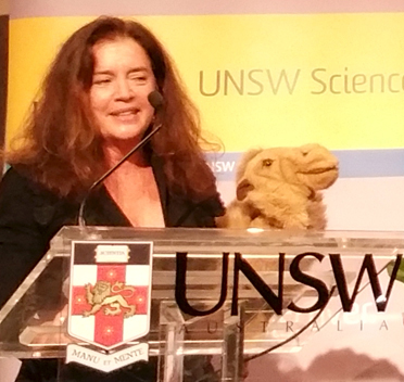 woman presenting at a podium with a camel puppet
