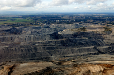 An aerial view of a large open cut mine showing black coal with farmland in the distance