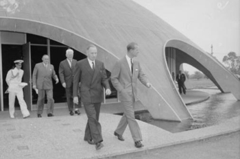 Prince Philip accompanied by dignatories walking across the bridge over the moat of the Shine Dome.