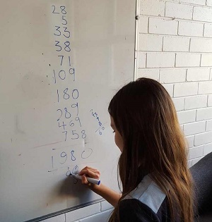 Female school student adding up numbers on a whiteboard