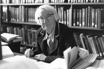 Dorothy Hill working at a desk with bookshelves behind