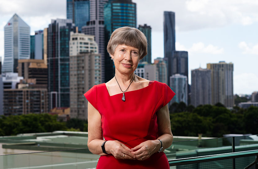 Lidia is smiling and wearing a bright red top while standing in front of a city skyline.