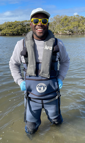 Smiling man wearing a wetsuit standing in knee-deep water