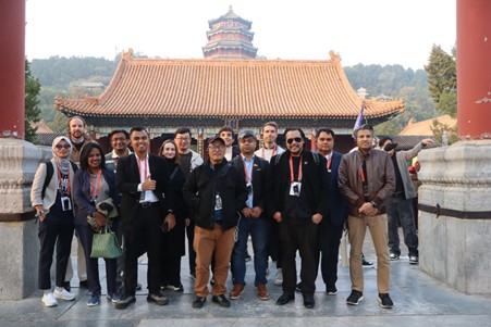 Group photo of people standing outdoors in front of a traditional Chinese building with ornate tiled roofs and a pagoda in the background.