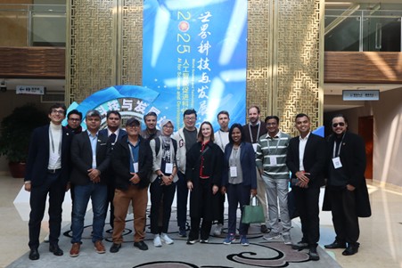 Group photo of 15 people is business-casual attire standing indoors in front of a large blue banner with Chinese text and the year 2025.