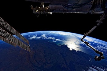 Blue planet Earth in background surrounded by black space, with parts of International Space Station visible in foreground