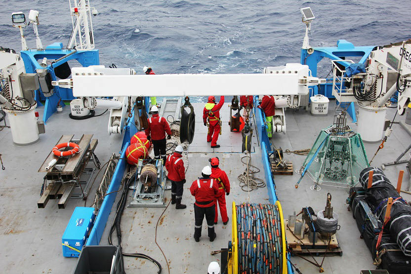 Stern of large ship, with people in wet weather gear using ship equipment