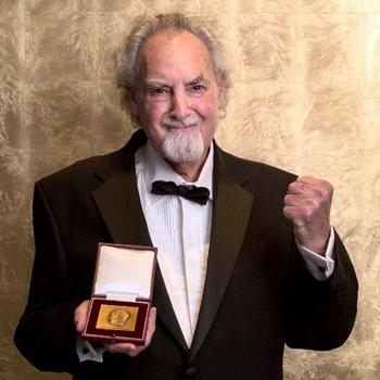 Smiling man holds a medal in one hand, while he clenches his other hand in a fist to represent victory