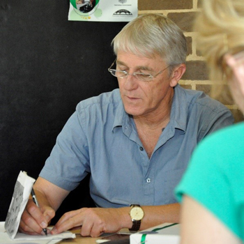 Man with reading glasses sitting at a table and writing, focused on what he's doing