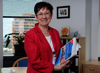 Shelley Peers in an office, holding Primary Connections teaching material and smiling