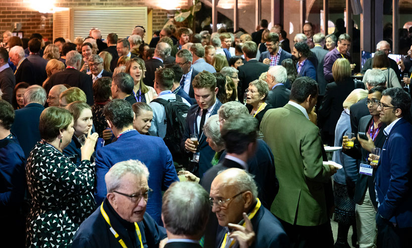 Large room packed with standing people smiling and talking to each other